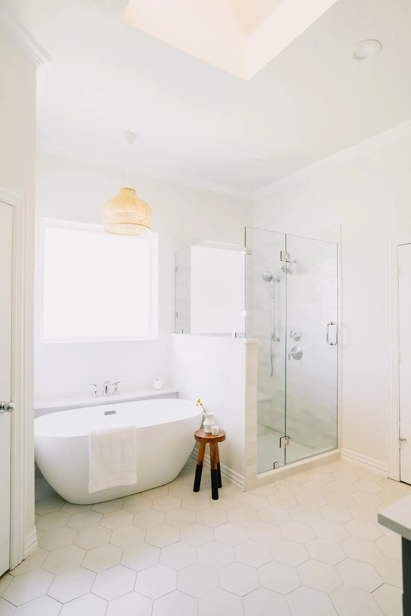 A remodeled primary bathroom in white, with a freestanding tub, a glass shower and hexagon tile floors