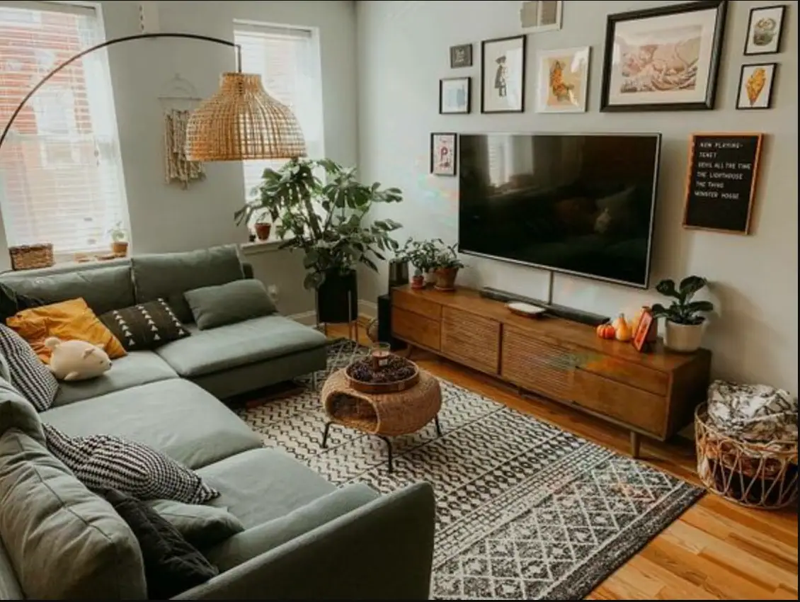 A relaxed living room with a sage green sectional, a rattan pendant, houseplants and a patterned rug