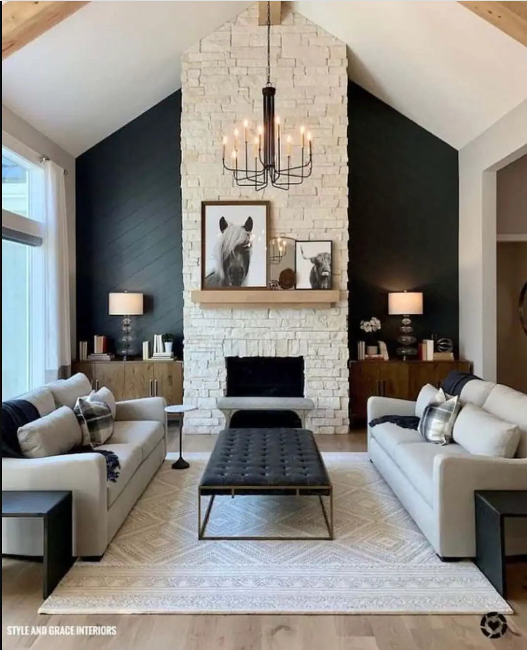 A vaulted living room with a white stone fireplace, black shiplap walls and a candle chandelier