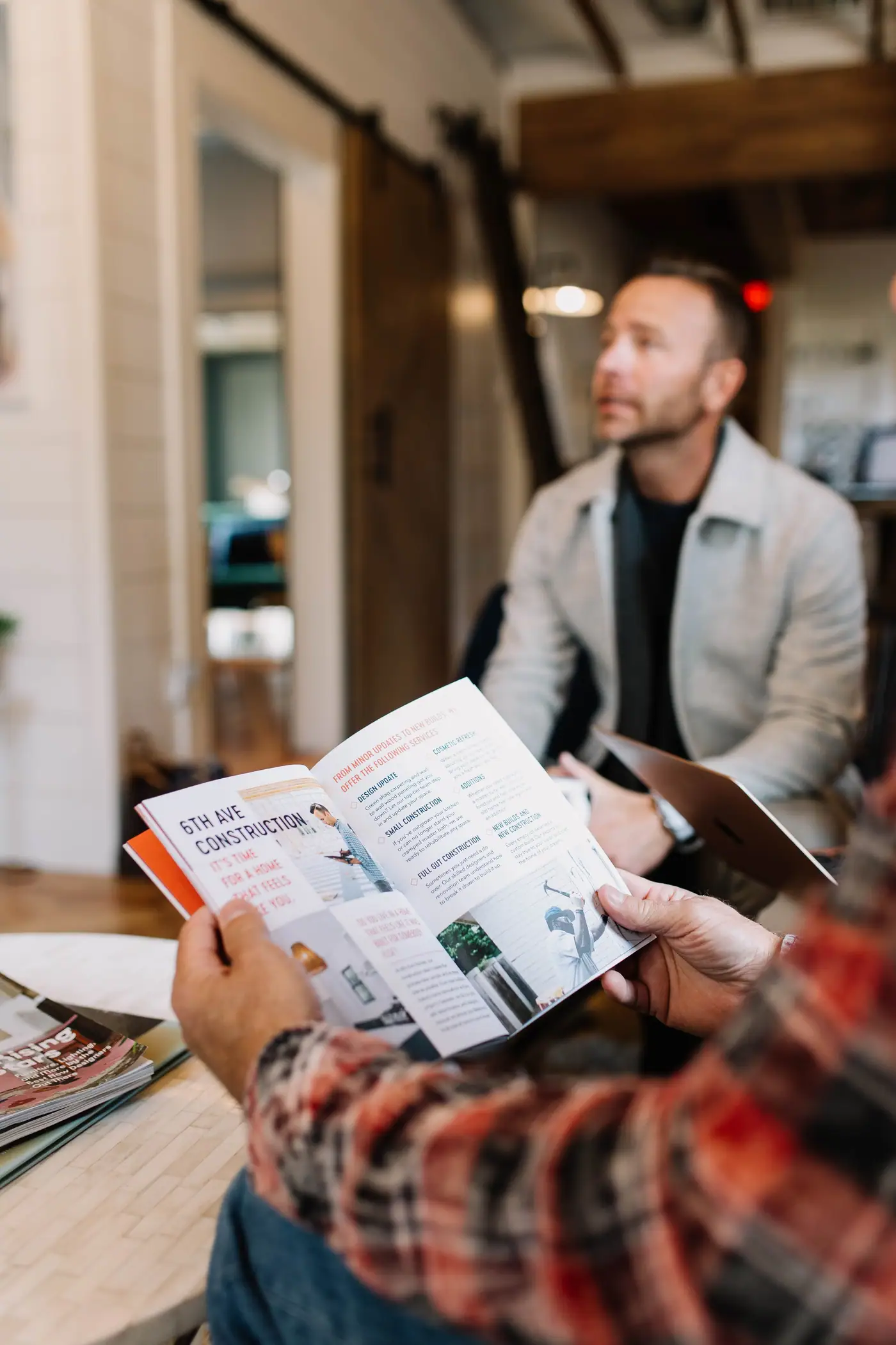 A client reading the 6th Ave Construction guide while a 6th Ave Homes team member talks through the options
