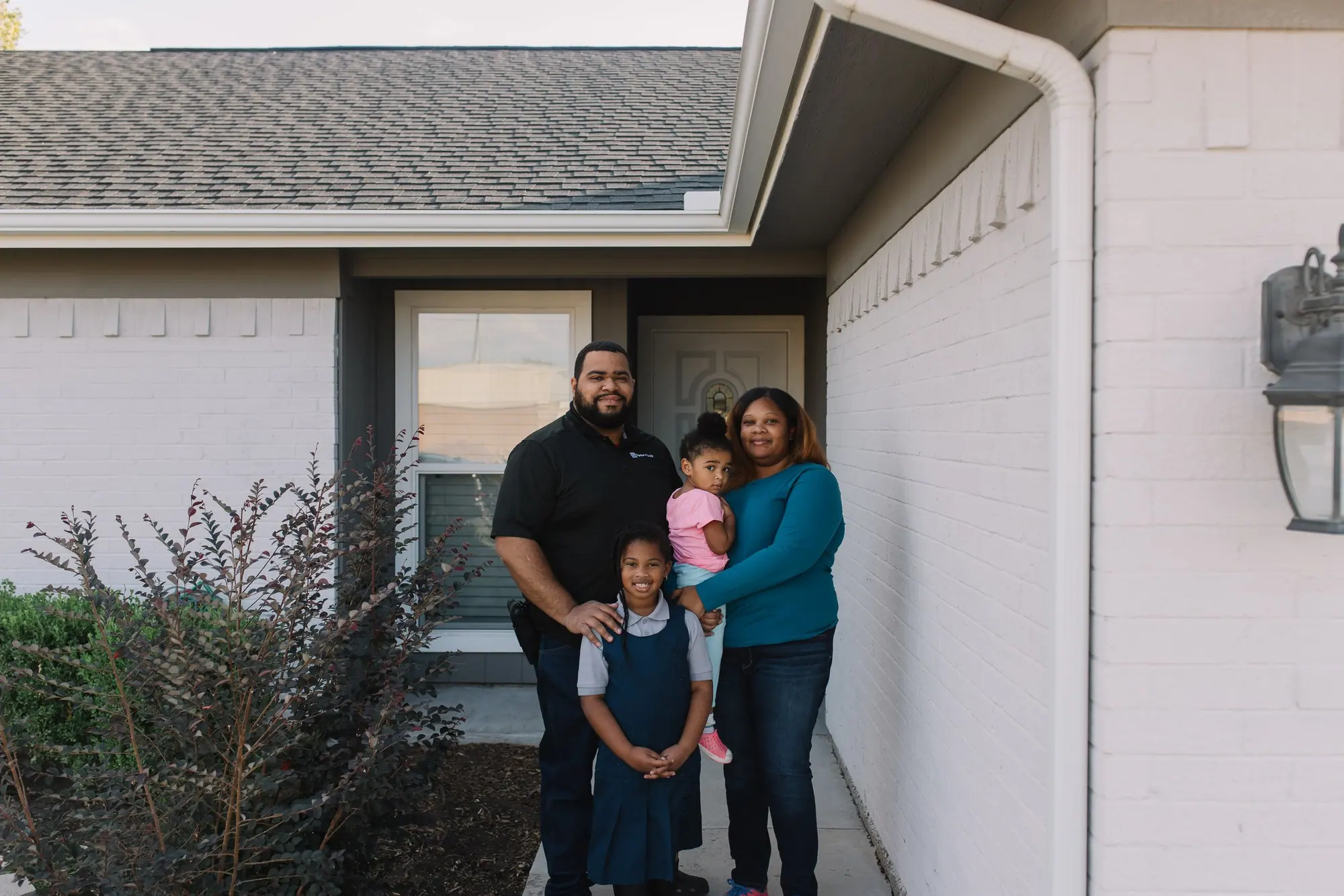 A Fort Worth family of four beaming on the front walk of the home they bought with 6th Ave Homes, in golden evening light