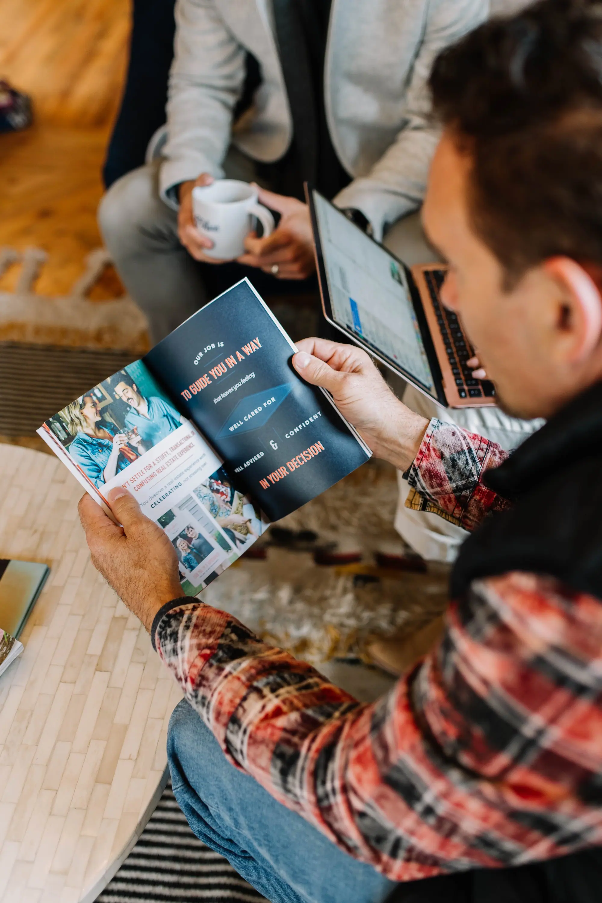 A 6th Ave Homes listing consult: the brochure page reading “our job is to guide you in a way that leaves you feeling well cared for,” with laptop and coffee
