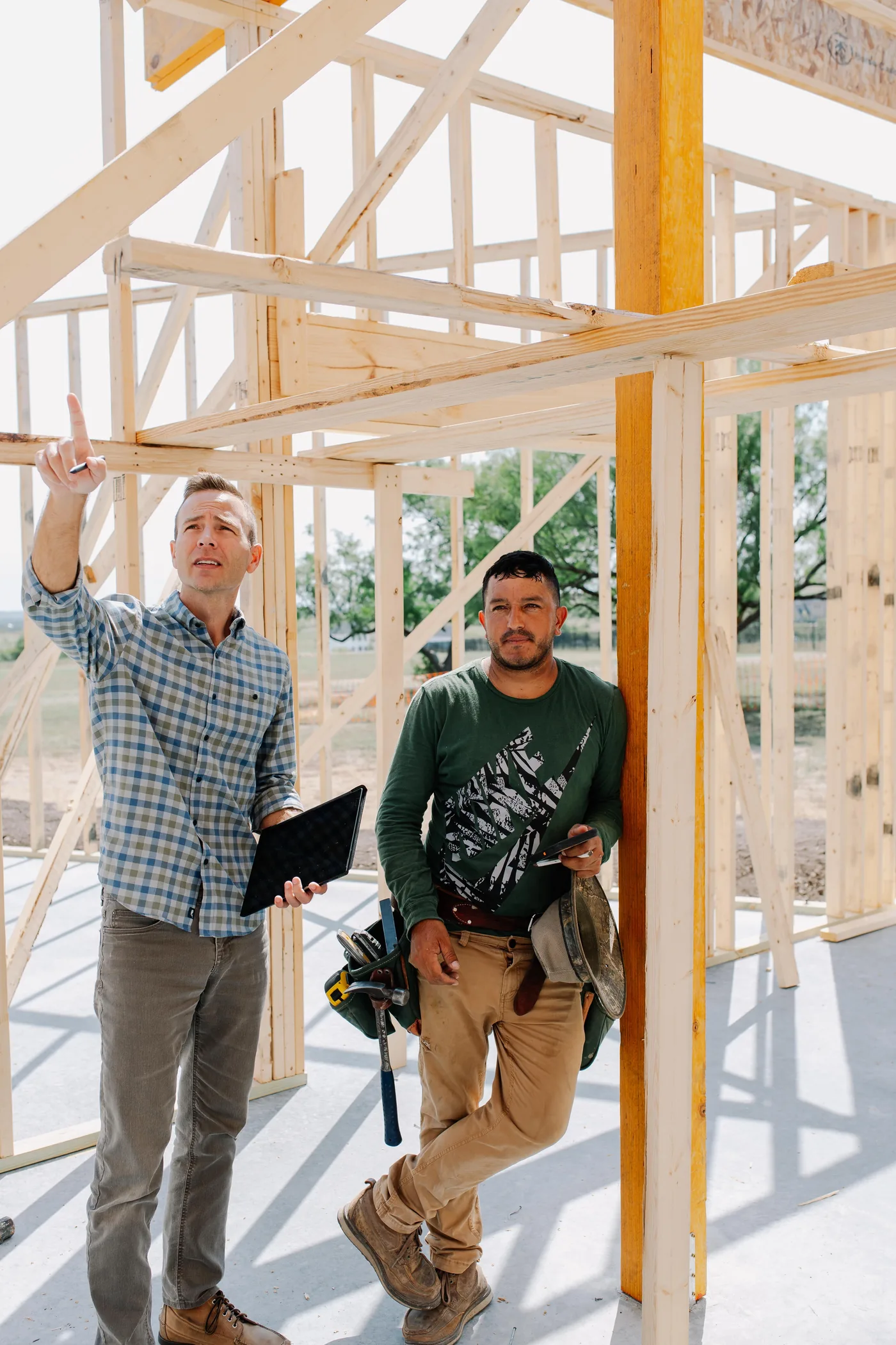 Two 6th Ave Homes team members inside a newly framed Fort Worth house, one pointing up at the structure