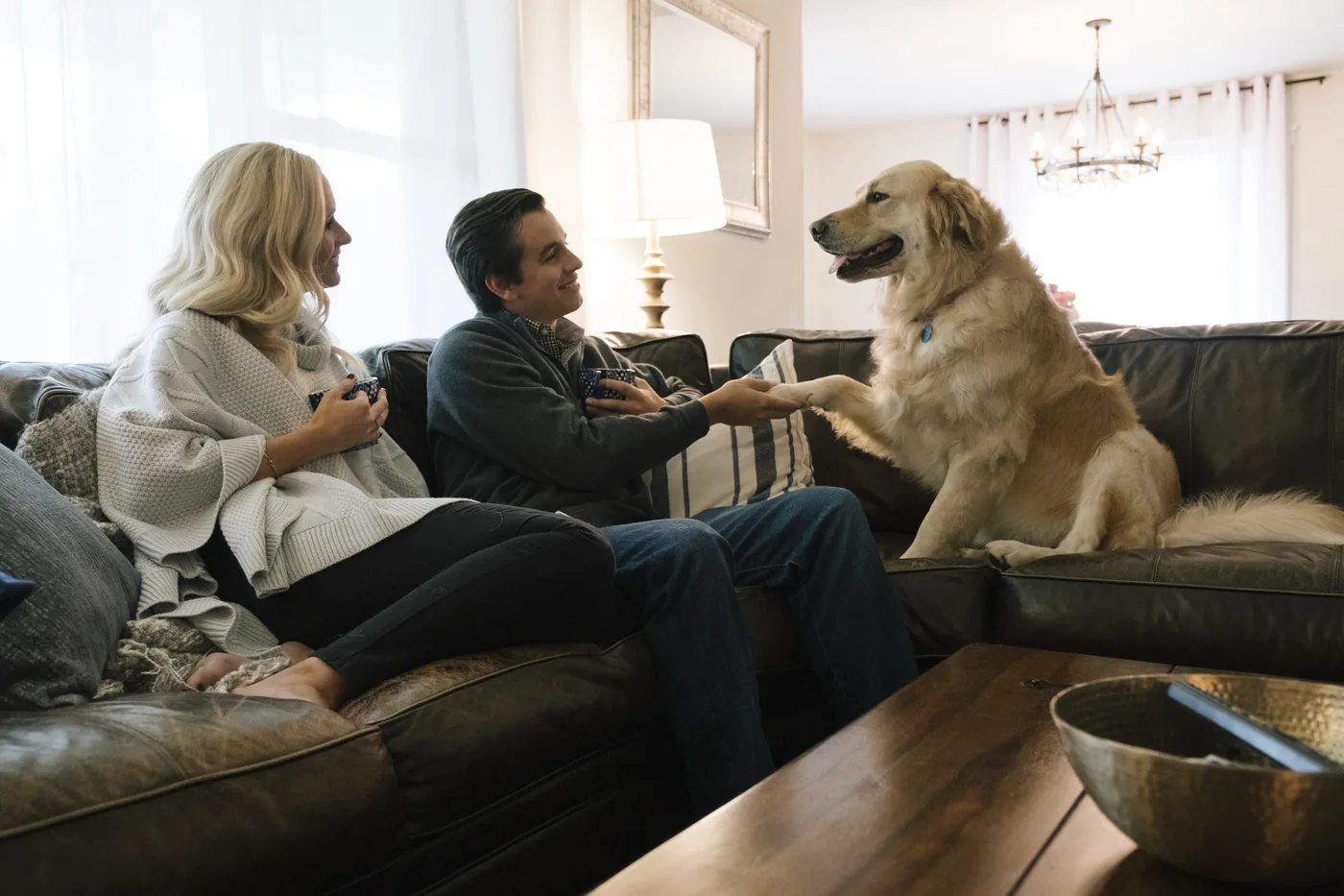 A couple and their dog relaxing on a leather sofa in their finished Fort Worth home
