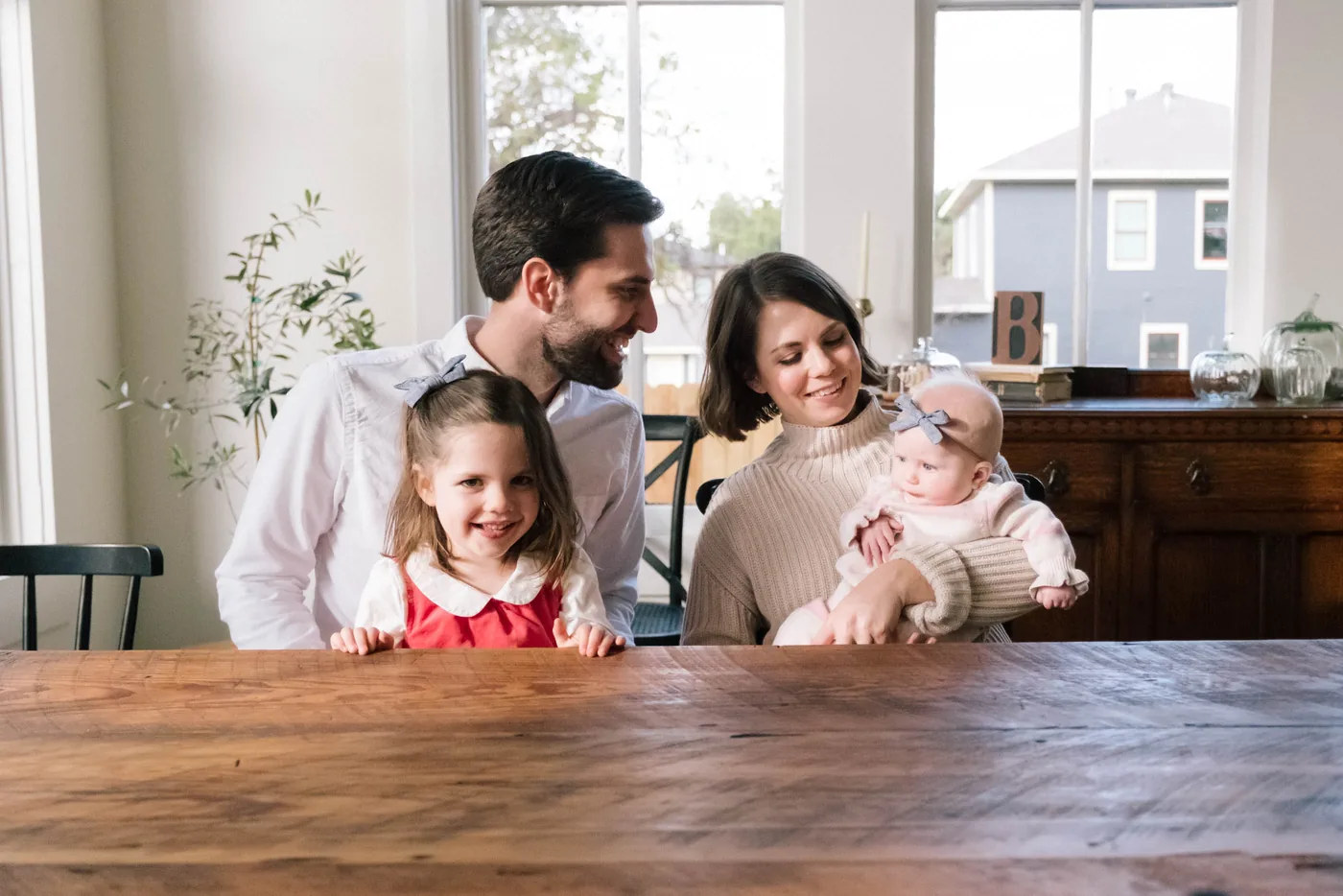 A Fort Worth family — two parents, a small girl and a baby — laughing together at their own dining table