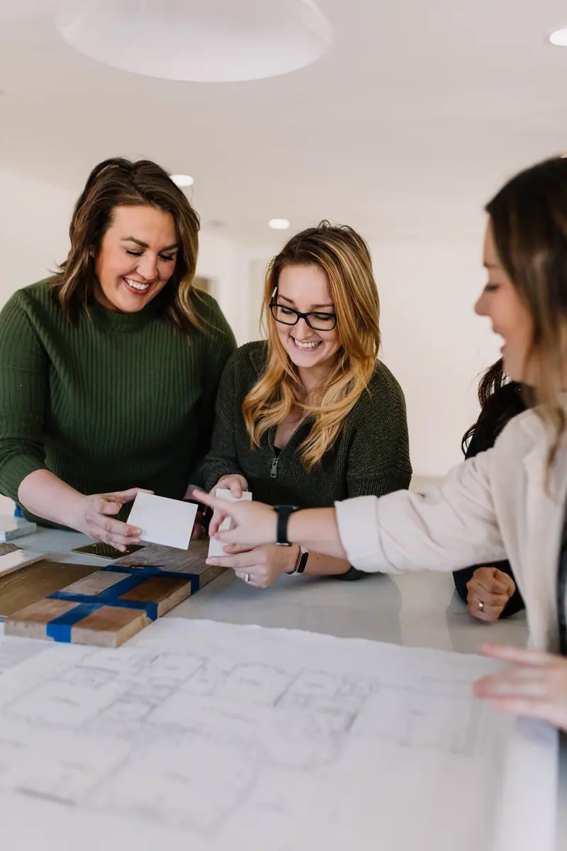 The 6th Ave Homes design team laughing over a floor plan and finish samples