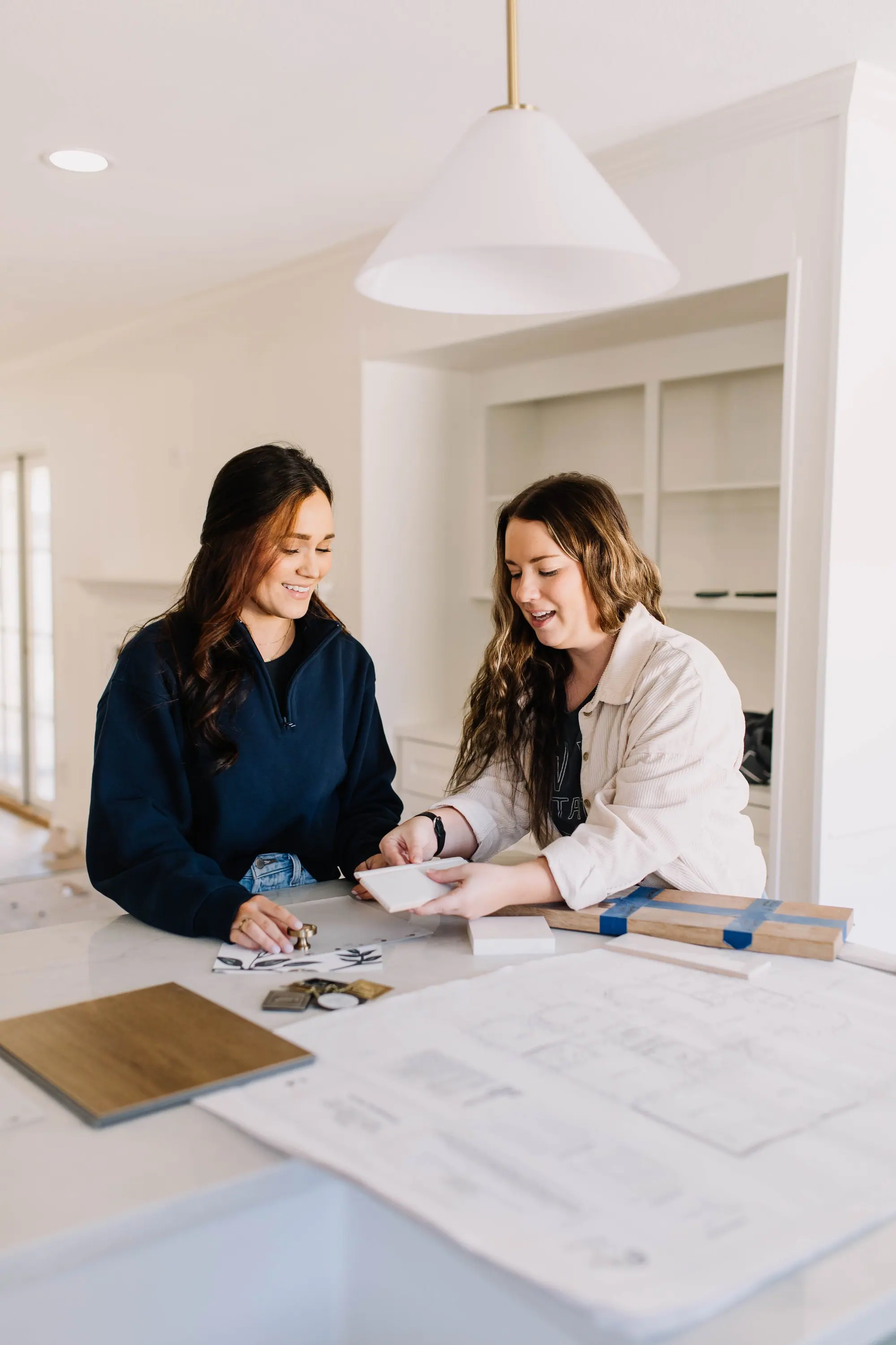 Two designers smiling over finish samples at the island of an in-progress Fort Worth remodel