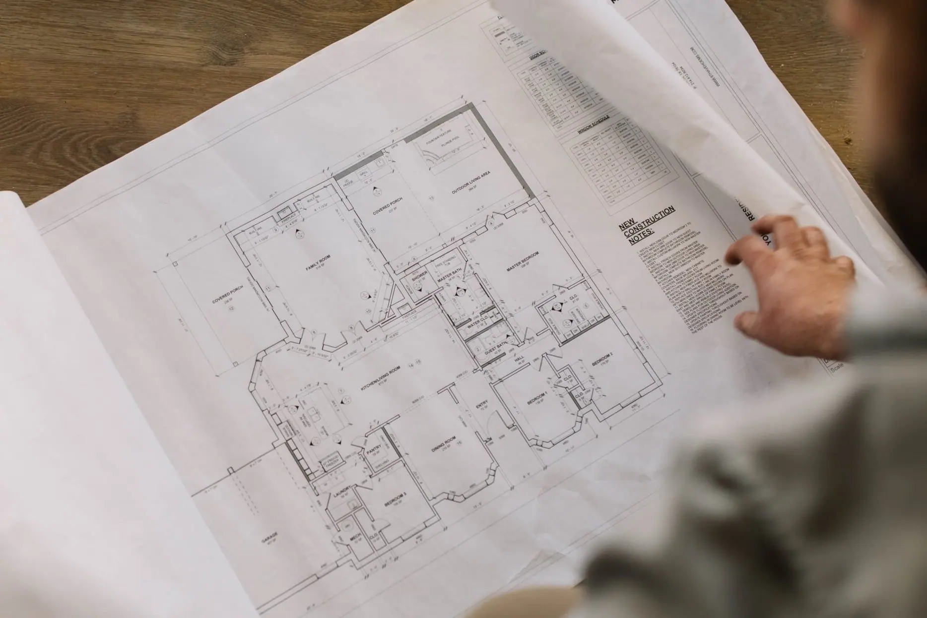 A 6th Ave Homes drafting team member reviewing a permit-ready floor-plan set with labeled rooms, a door and window schedule, and construction notes