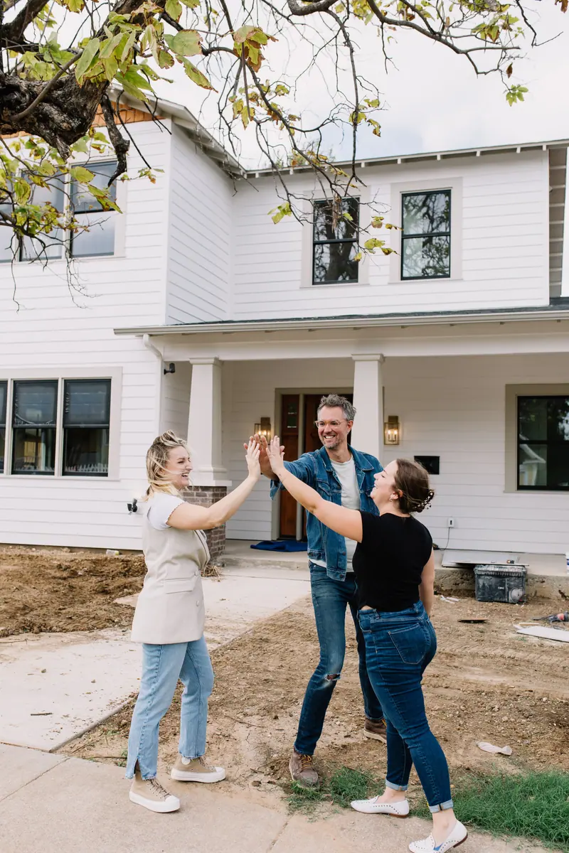 Three people high-five in front of a just-finished 6th Ave Homes new build in Fort Worth