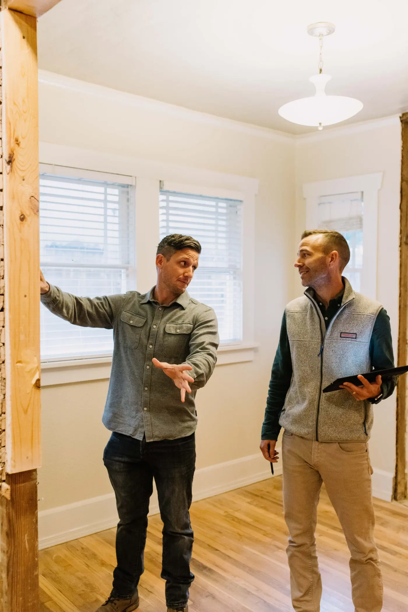 Two men in a room mid-renovation, one resting a hand on a wall opened down to its post, the other holding a tablet.