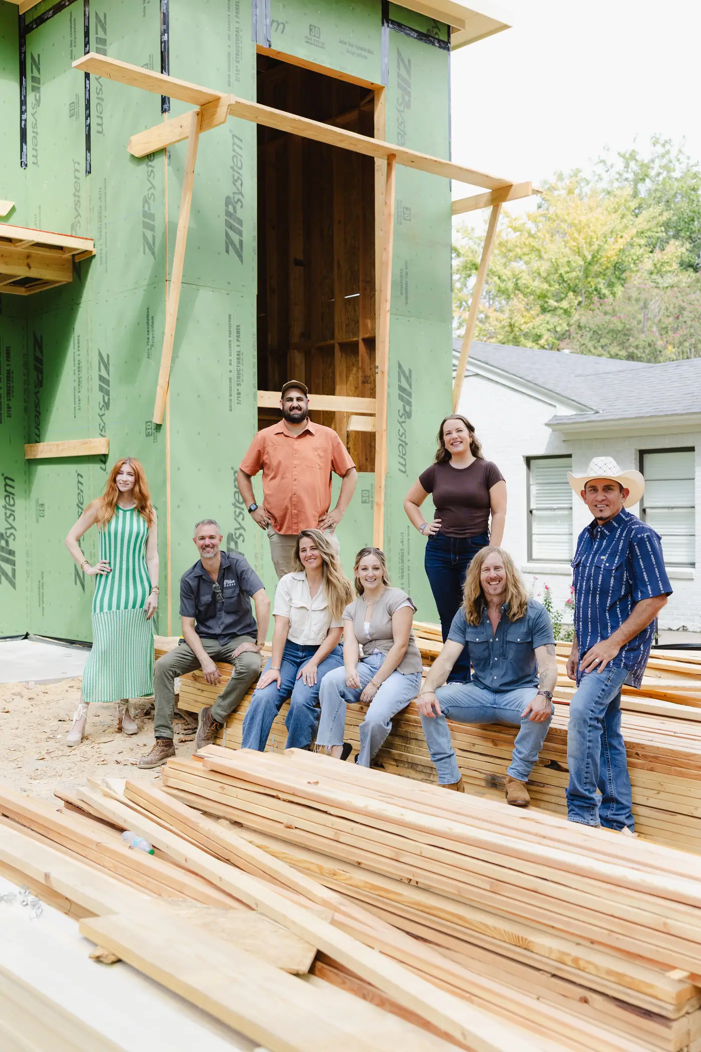 The 6th Ave Homes design and construction team gathered on a lumber pile in front of a framed Fort Worth new build