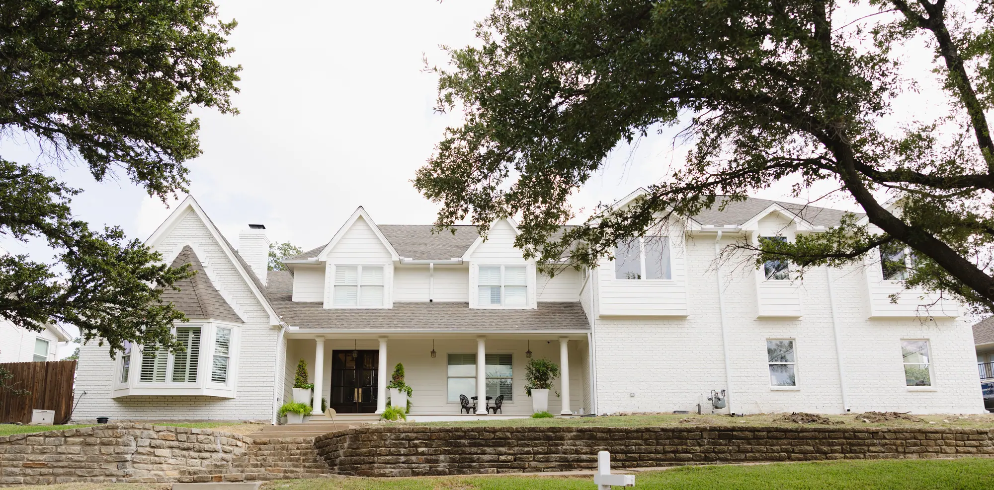 A white two-story Fort Worth home remodeled by 6th Ave Homes, under a sprawling live oak
