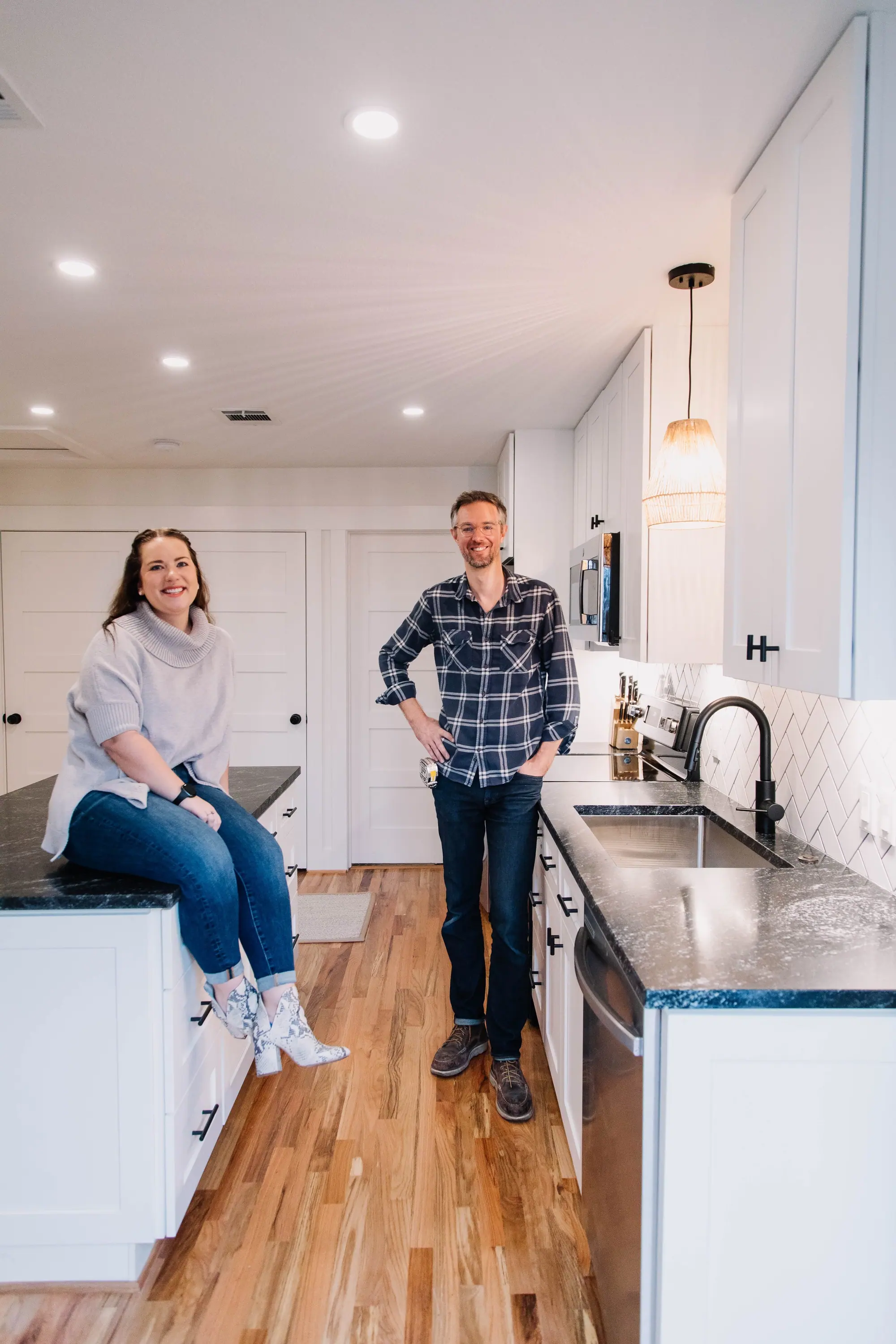 A Fort Worth couple in the white kitchen 6th Ave Homes remodeled for them, one seated on the island and one leaning against the counter