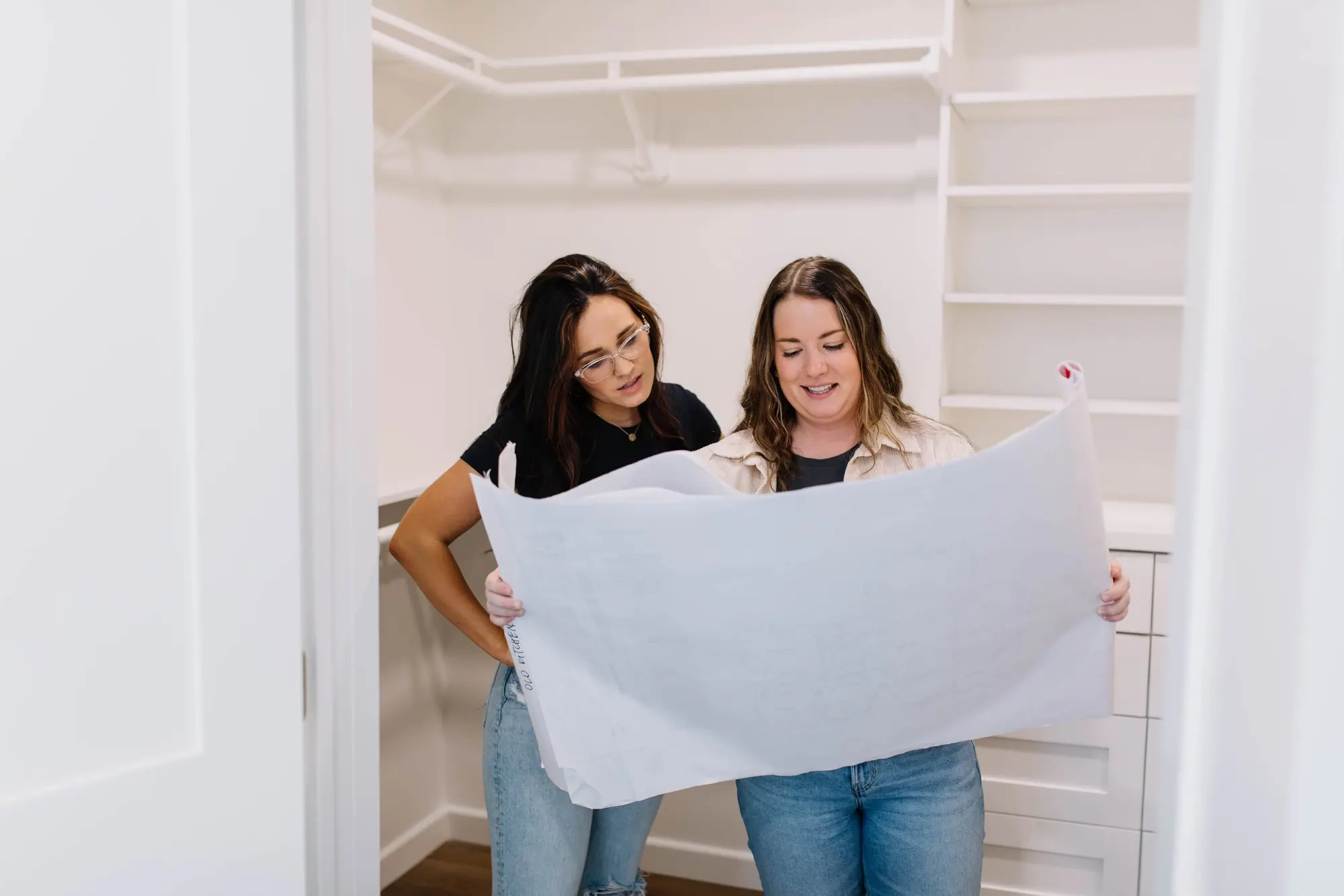Two members of the 6th Ave Homes design team unrolling a large tracing-paper plan inside a newly finished walk-in closet.