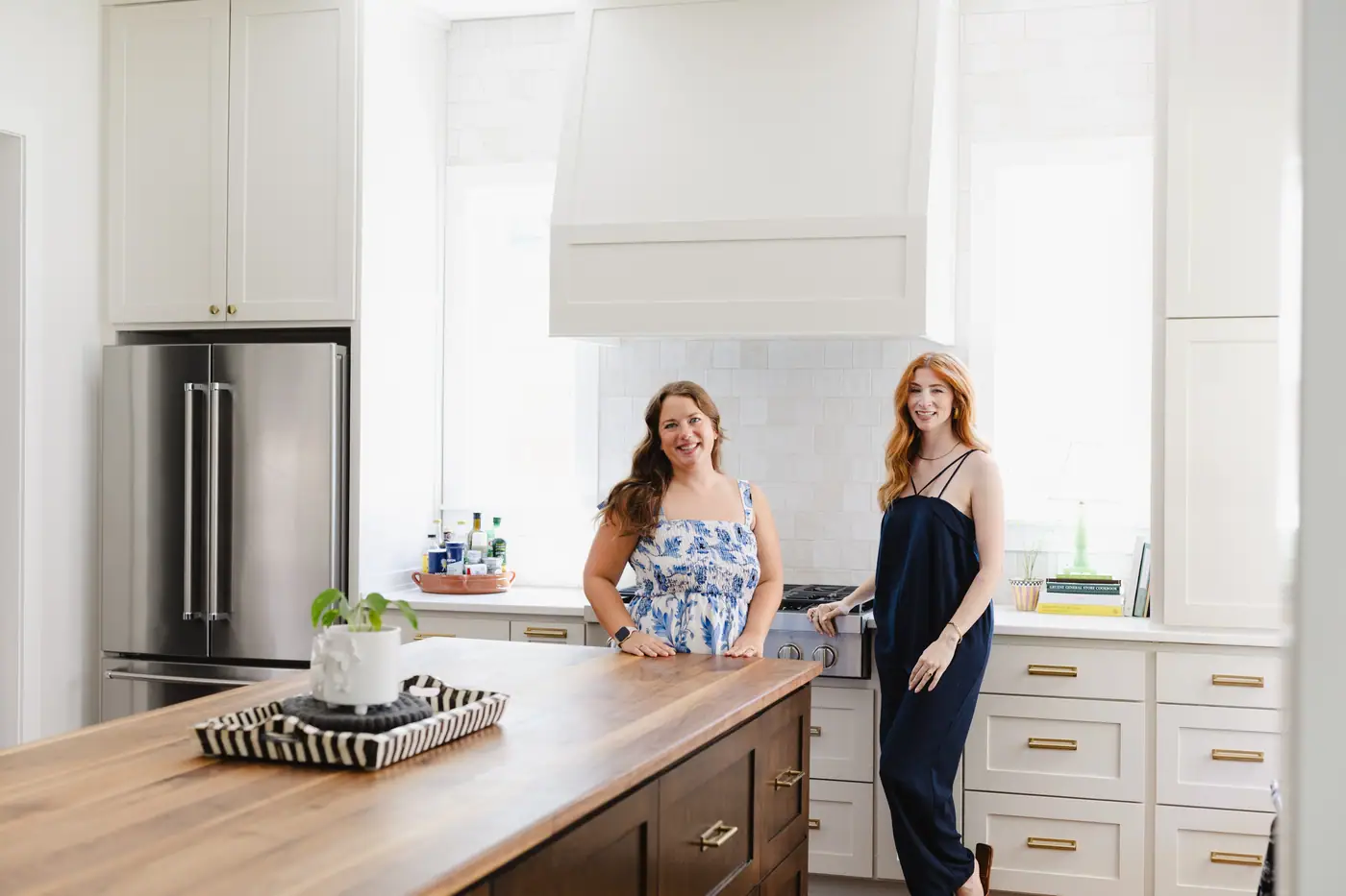 Two 6th Ave Homes team members smiling in the finished white kitchen of a Tanglewood custom home in Fort Worth, beside its wood-topped island