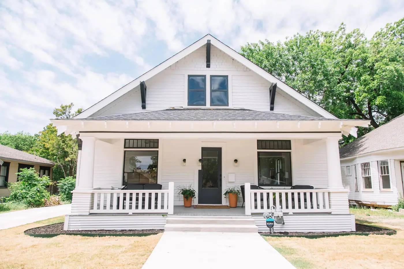 A freshly refreshed white Craftsman bungalow with a deep columned porch, black door, and mature landscaping in Fort Worth by 6th Ave Homes