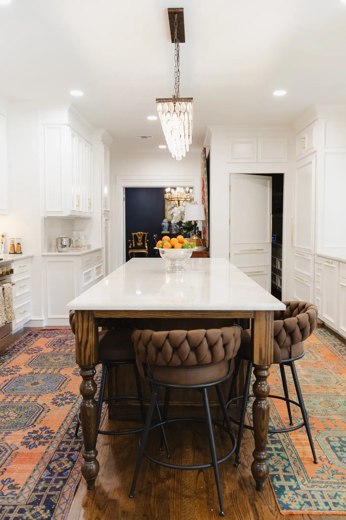 A white Fort Worth kitchen with a turned-leg walnut island, woven leather stools, and vintage rugs designed by 6th Ave Homes