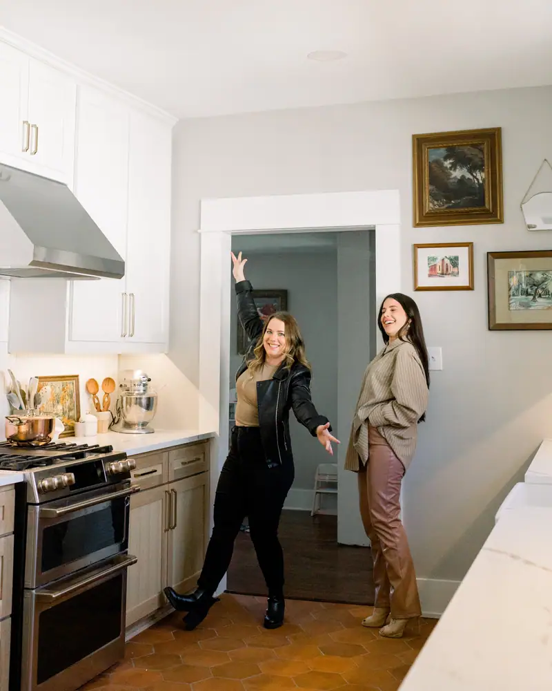 Two 6th Ave Homes team members walking through a finished Fort Worth kitchen together, one gesturing through a wide cased opening while the other listens