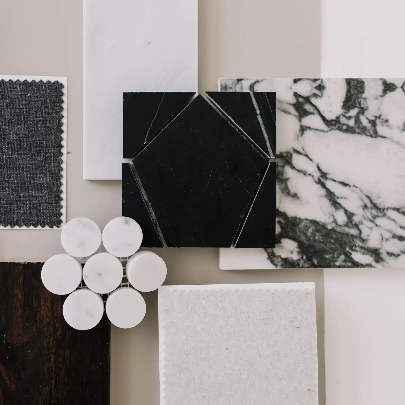 A material board laid out flat: veined marble, honed black stone, hexagonal white tile, dark stained oak, and two upholstery swatches