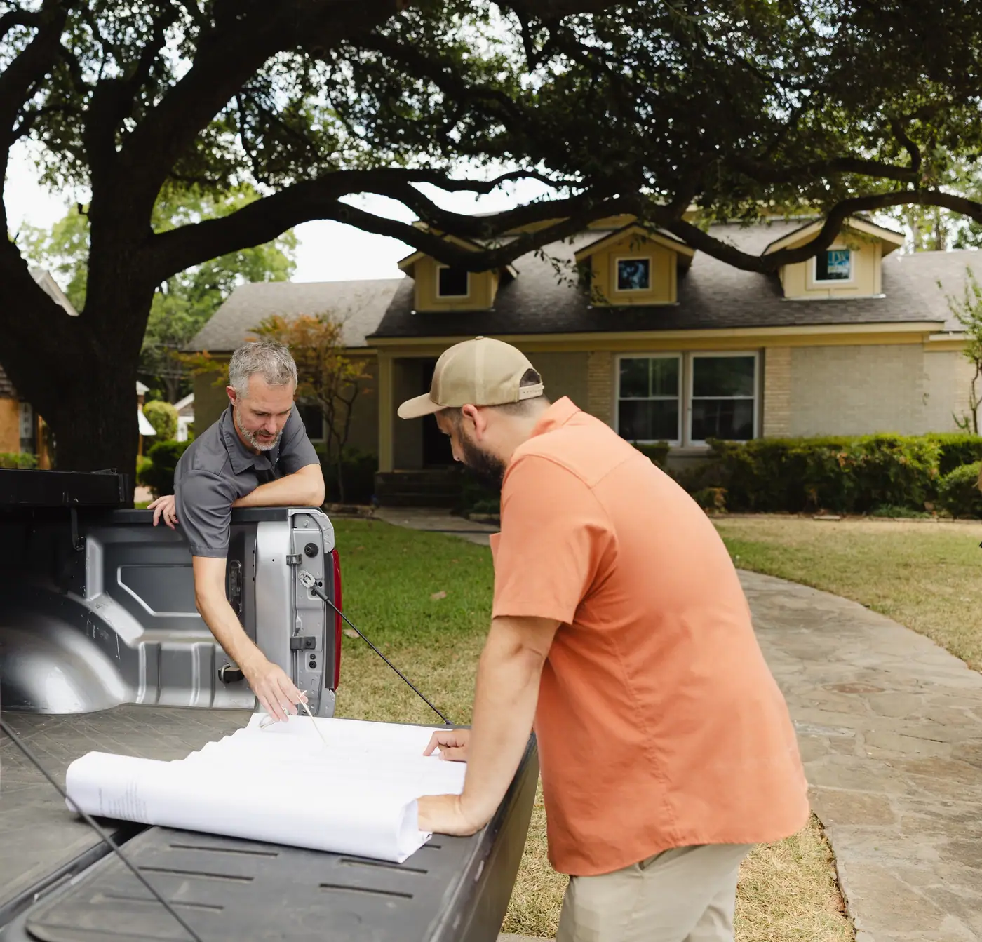 Two 6th Ave Homes team members going over a plan set on a pickup truck’s tailgate under a live oak