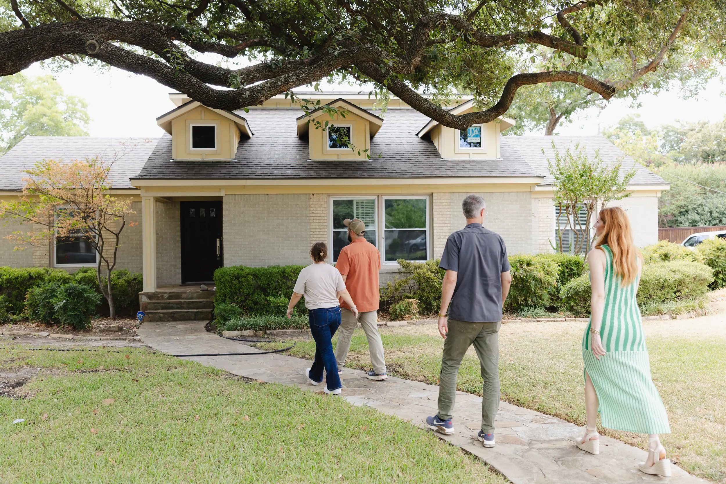 People walking up to a ranch house under a live oak.