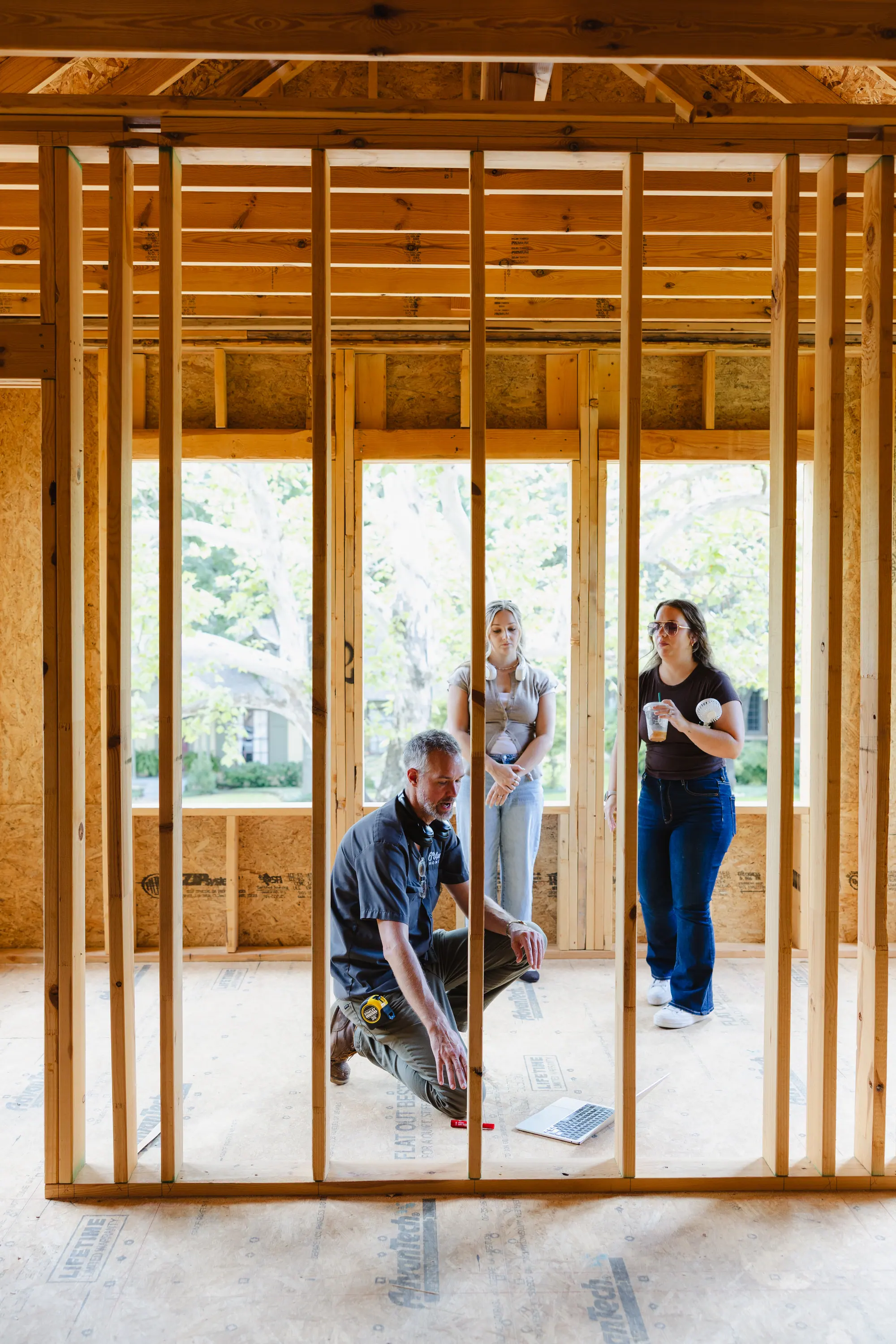 Three of our team in a newly framed room, one kneeling to point something out on the subfloor.