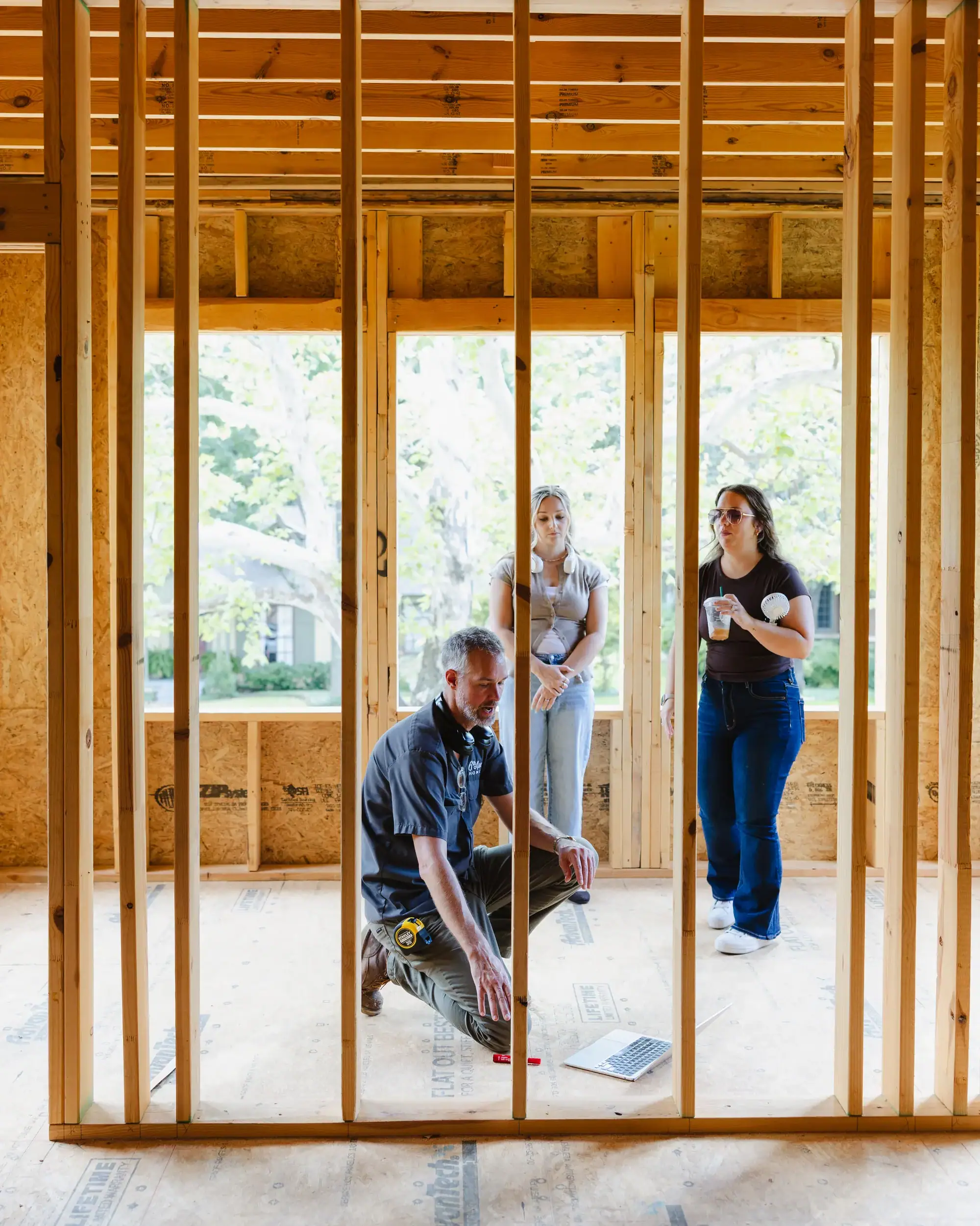 Three 6th Ave Homes team members inside the framing of a custom home under construction in Fort Worth, one kneeling on the subfloor and two standing behind him
