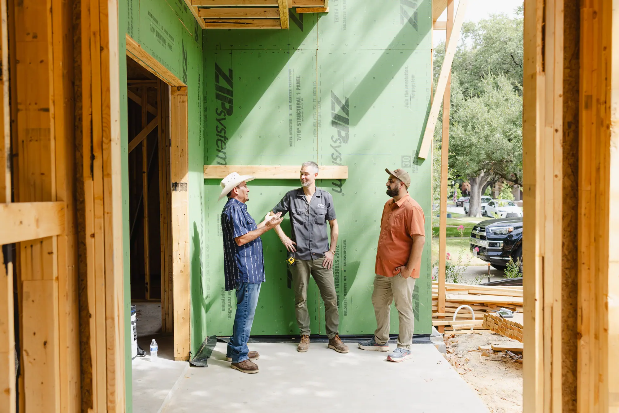 Three of our team talking in the open garage bay of a new house, against green sheathing, framed by bare studs.