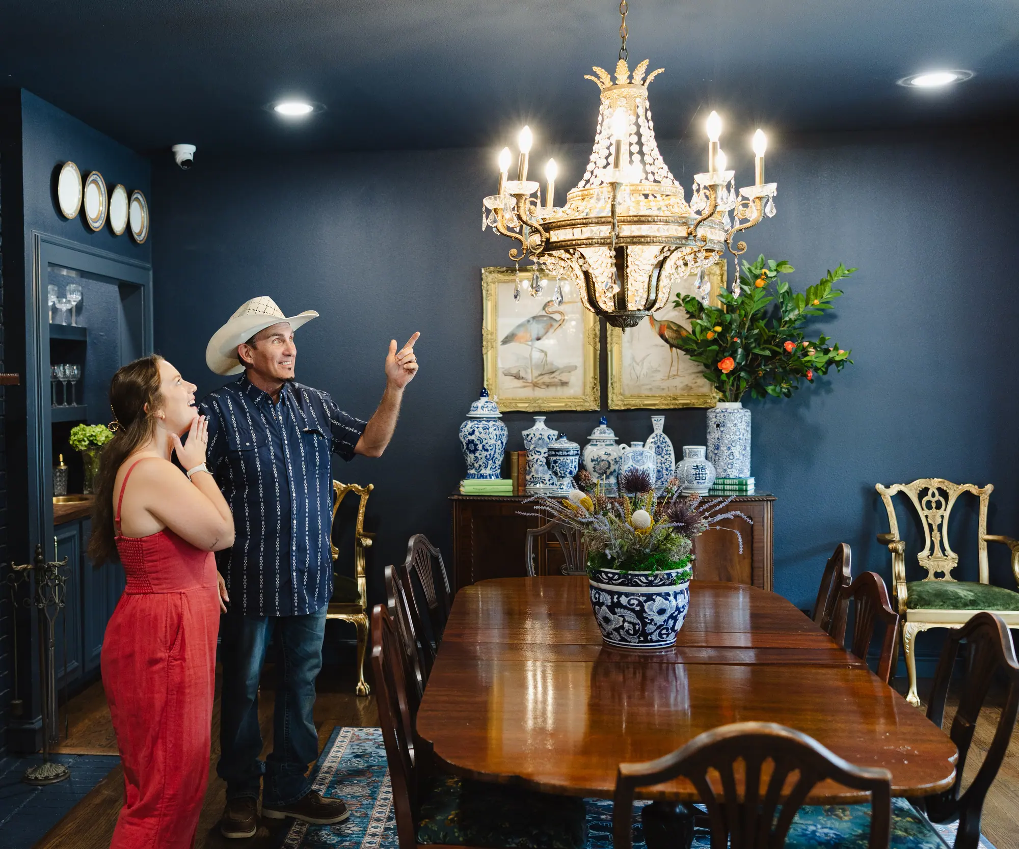 Two of our team look up at a crystal chandelier in a navy dining room, one pointing to it, the other with a hand at her chin.