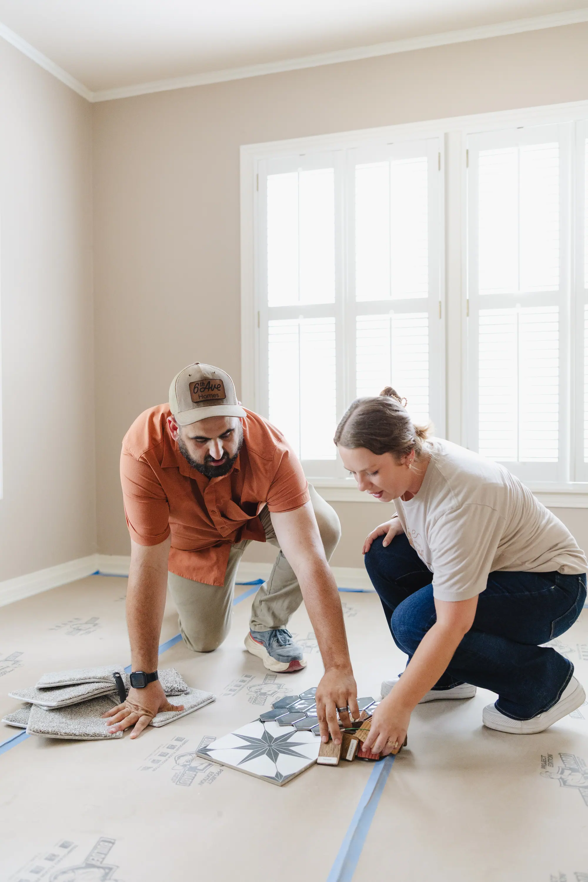 Two of our team down on a paper-covered floor in an empty room, choosing among hexagon tile, a star-pattern tile, wood samples and carpet squares.