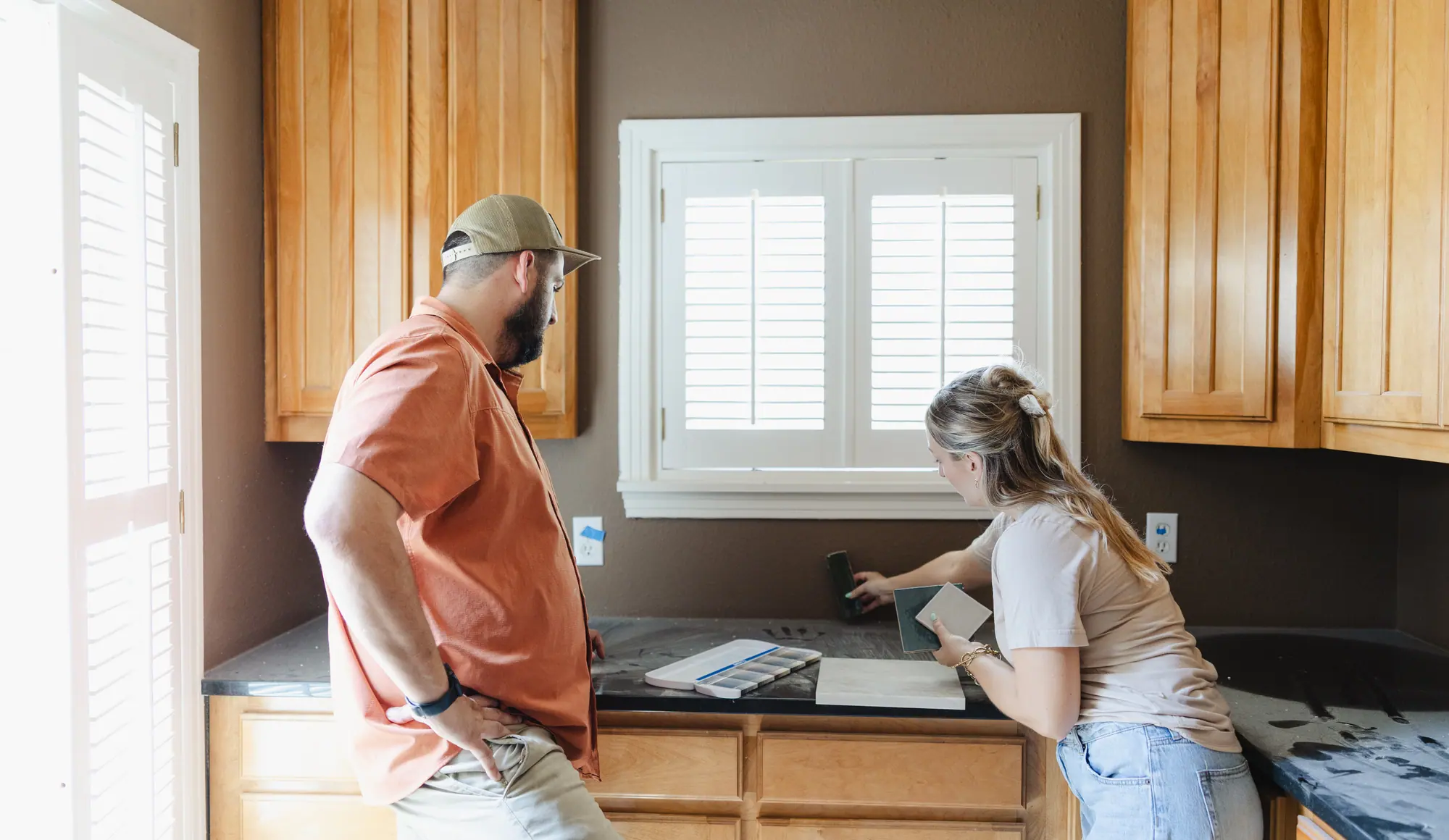 Two of our team testing backsplash tile samples in an older kitchen with honey-toned wood cabinets