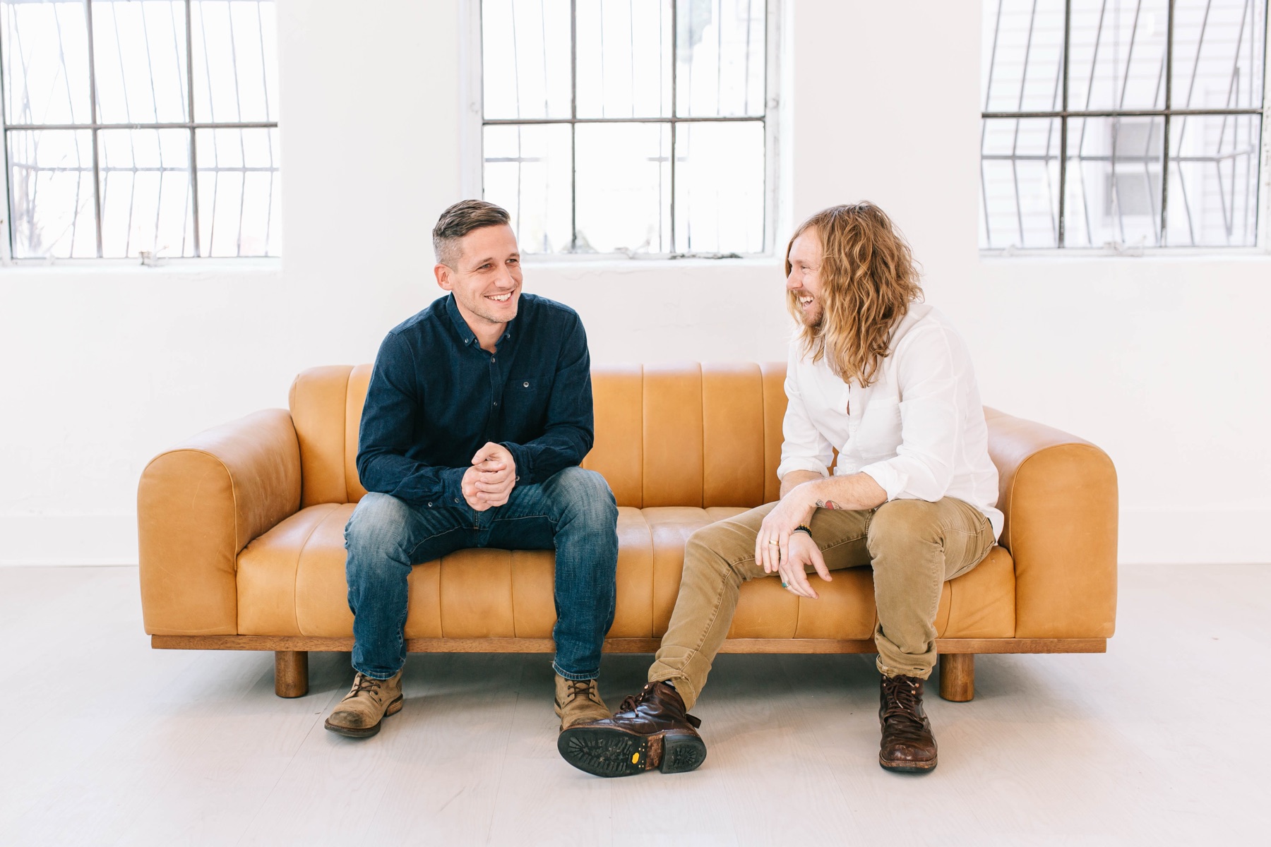 6th Ave Homes founders Jimmy Williams and Jamey Ice laughing together on a leather couch in their Fort Worth studio