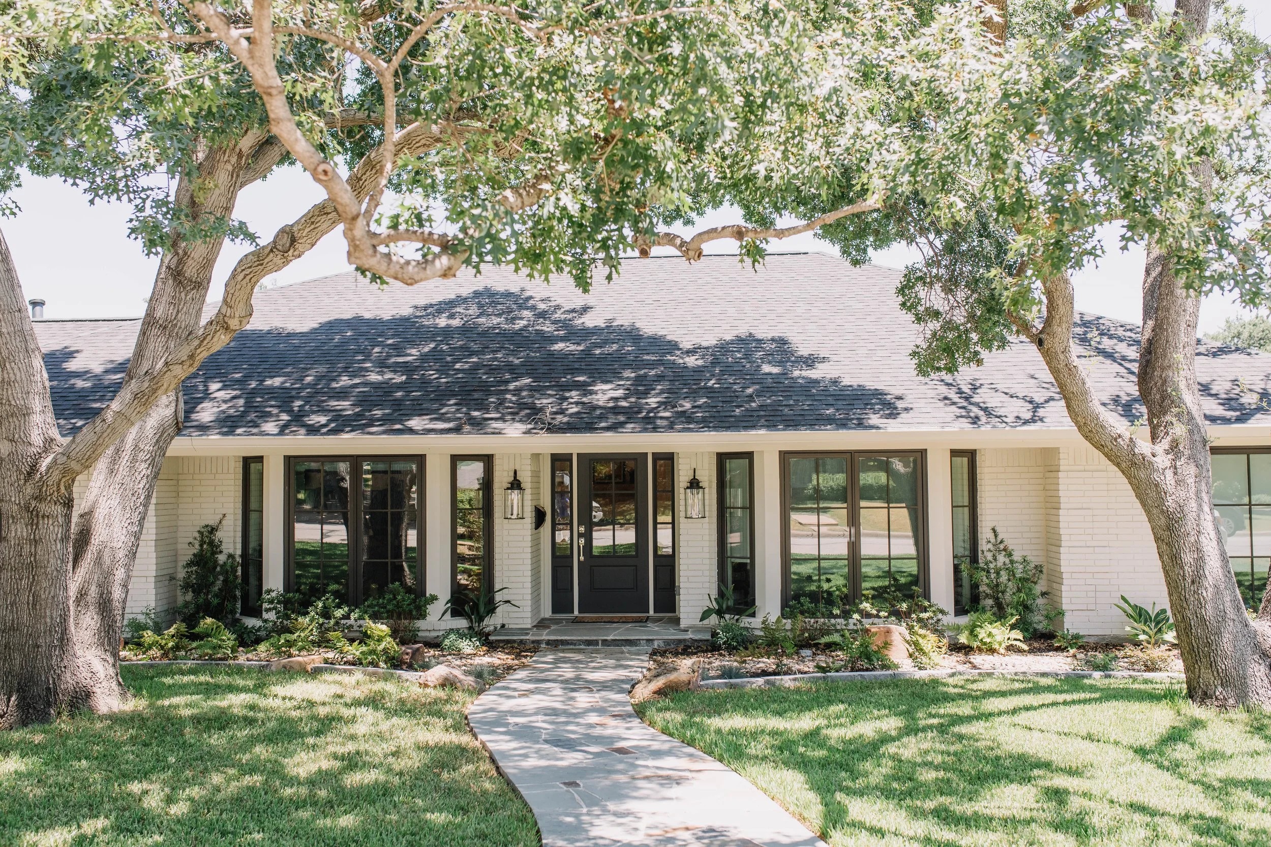 A white-brick Fort Worth home beneath two sprawling live oaks, restored by 6th Ave Homes