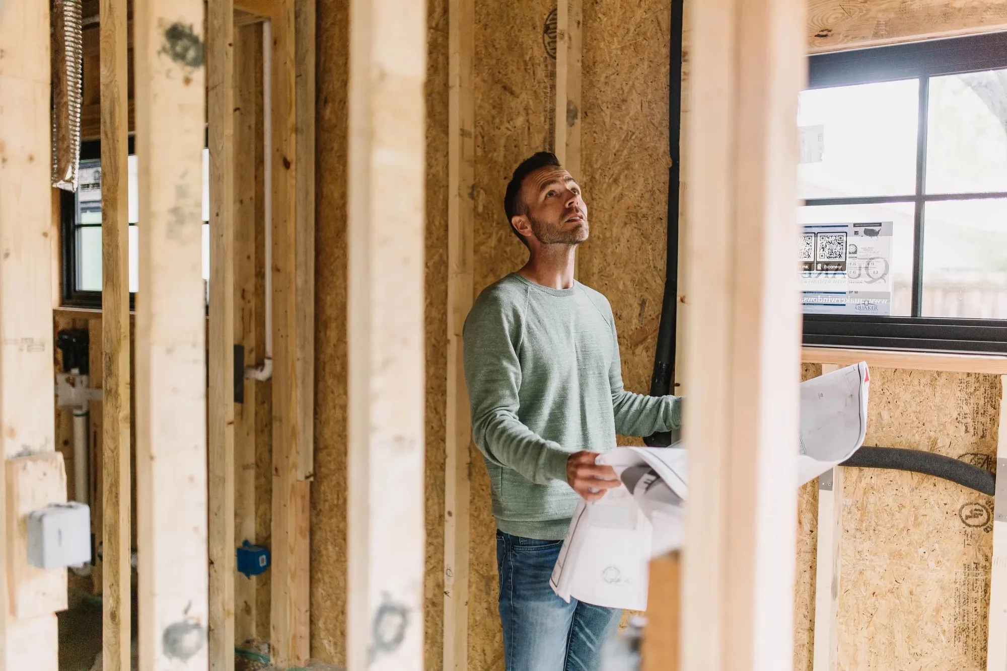 A 6th Ave Homes team member reading a plan set inside the framing of an addition