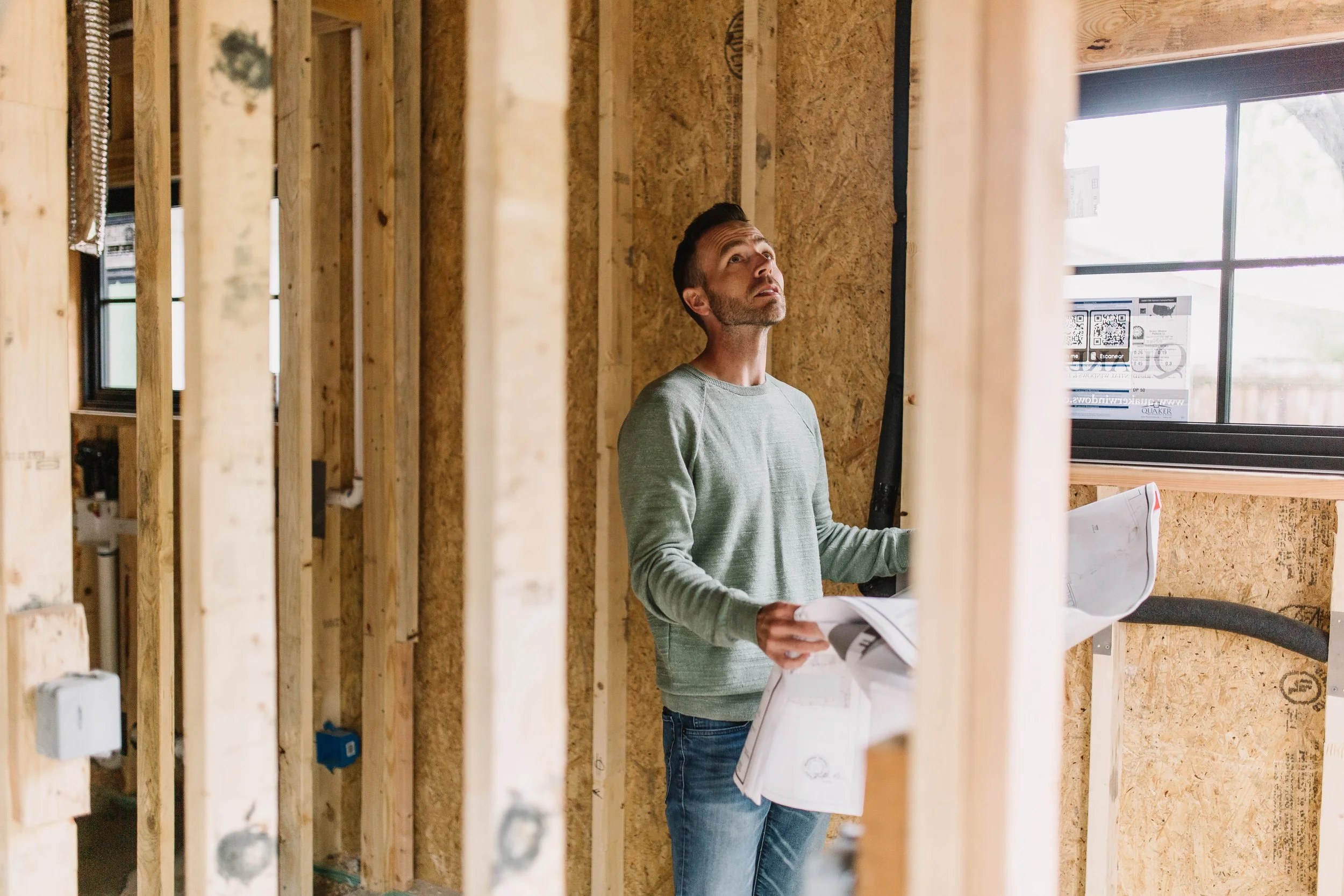 A 6th Ave Homes team member standing inside a framed-out addition, reading the permit set