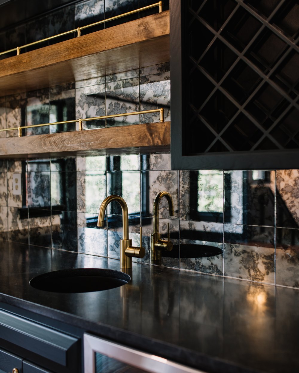 Moody wet bar with antiqued-mirror tile, brass gooseneck faucets, and a black stone counter on Fort Worth's Near Southside