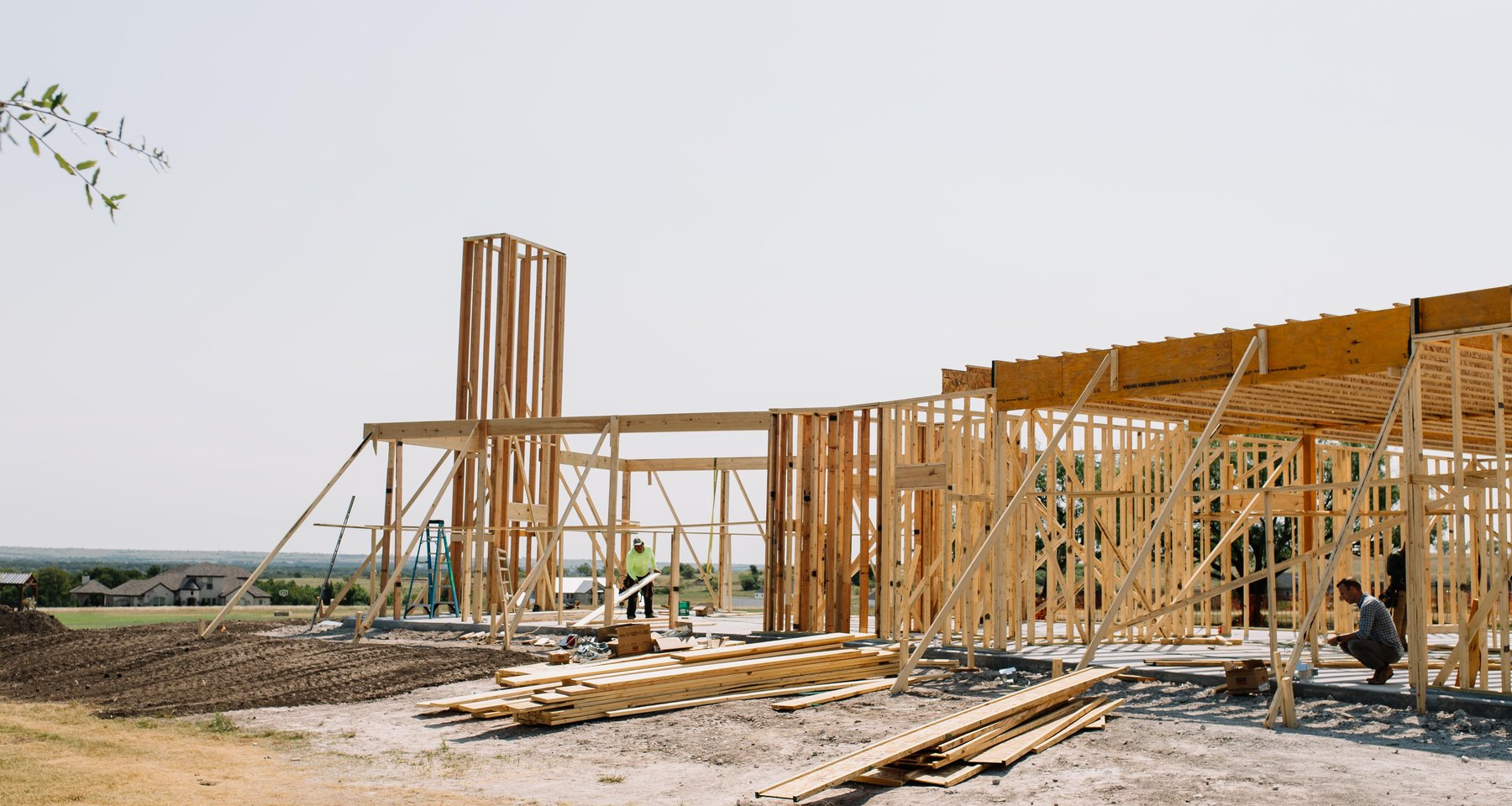 A custom home under construction in Fort Worth, framed and open to the sky, with a carpenter working on the deck