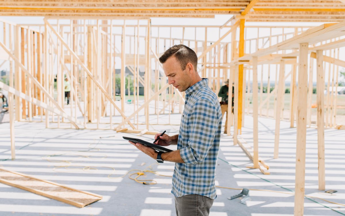 A 6th Ave Homes project lead taking notes on a tablet inside the frame of a custom home under construction