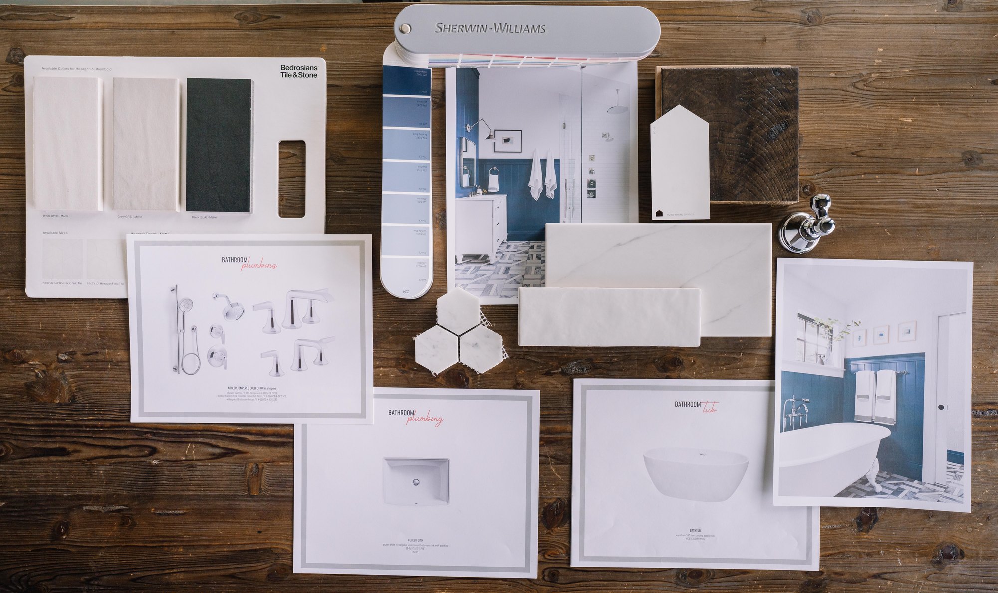 A design deliverable laid out on a wood table: paint deck, tile and stone samples, marble hex, and printed plumbing and tub specification sheets