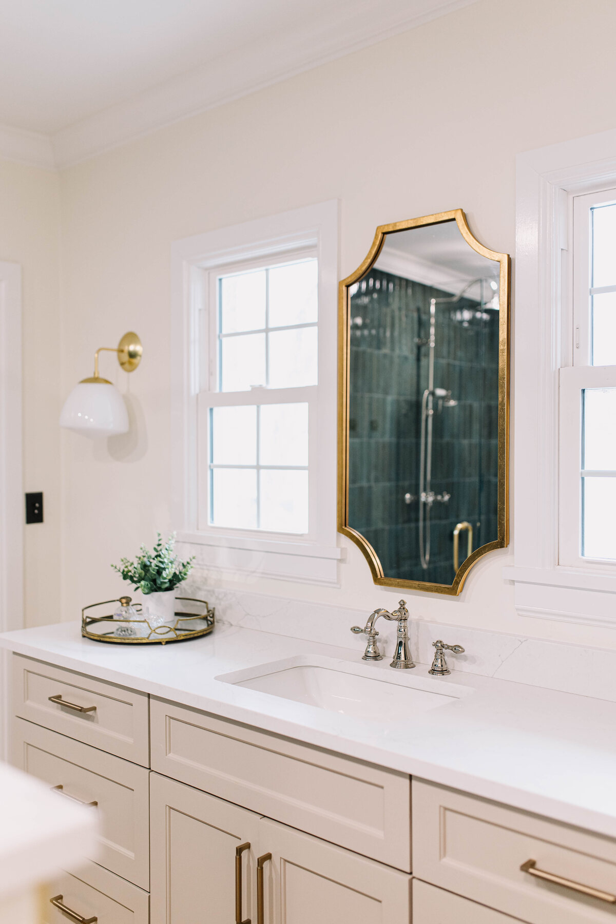 A Fort Worth vanity designed by 6th Ave Homes, its gold mirror reflecting a green-tiled shower