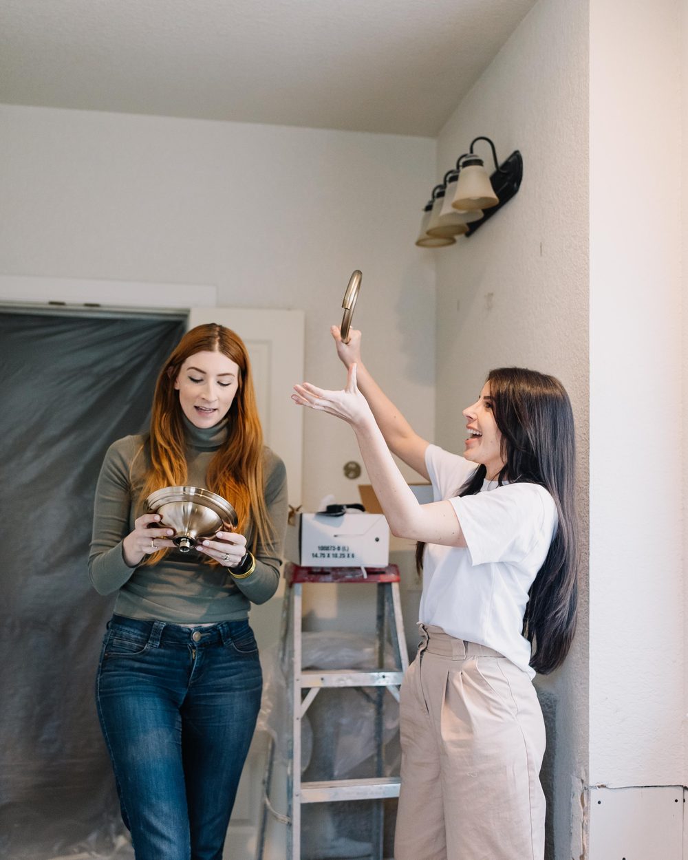 Two 6th Ave Homes designers hanging a brass light fixture inside a Fort Worth home mid-renovation