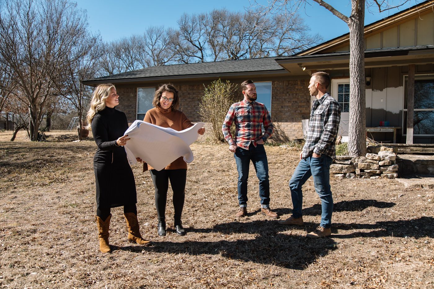Two 6th Ave Homes team members reading a set of plans with homeowners in the front yard of a Fort Worth ranch house