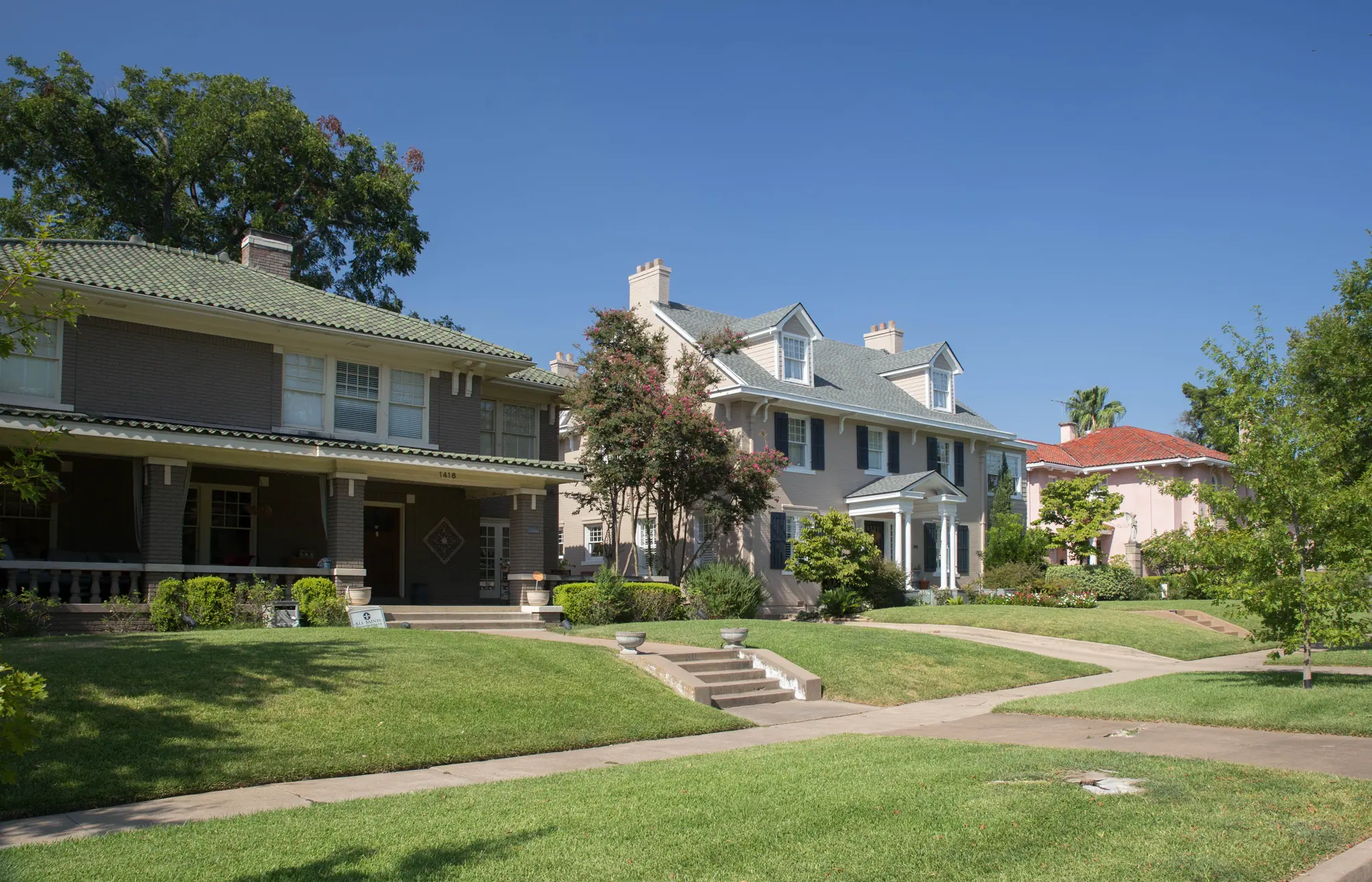 Two large older houses behind terraced front lawns and concrete steps, with a parkway and sidewalk in front.