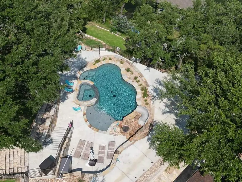 Aerial view through oak trees of a free-form pool with spa and slide