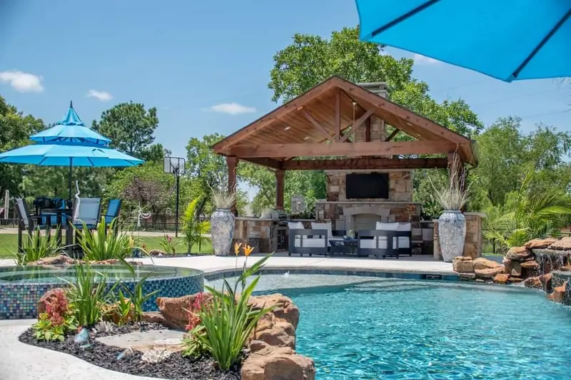 A covered pavilion with fireplace and TV behind a pool and spa