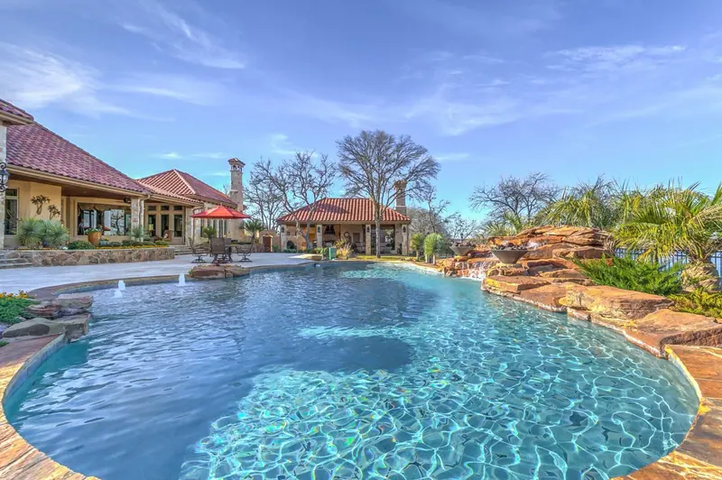 Free-form pool with rock grotto, fire bowls, and a red-tile cabana