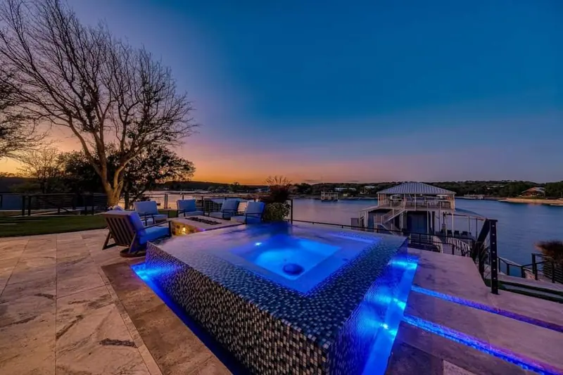 A glass-tile raised spa spilling over an infinity edge at sunset