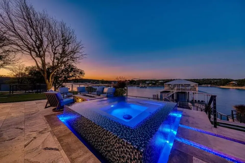 A glass-tile raised spa spilling over an infinity edge at sunset