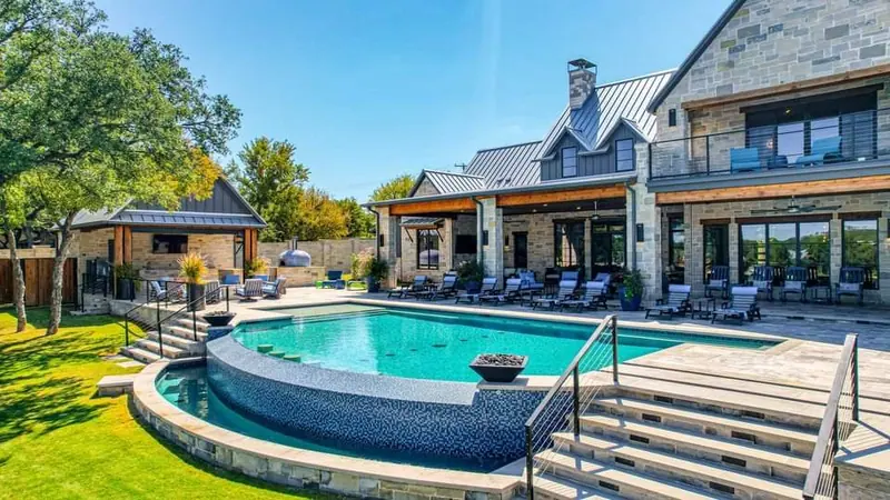 Infinity pool with swim-up stools in front of a stone pool house with a pizza oven