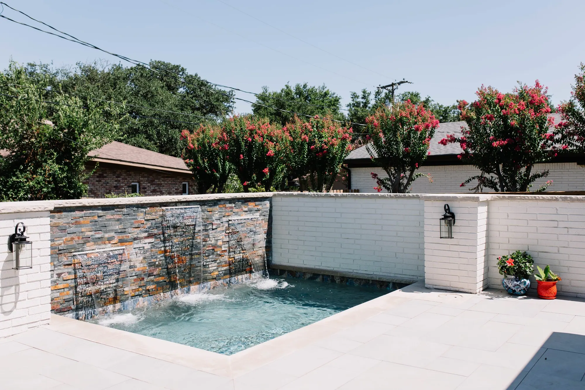 An in-town Fort Worth plunge pool with a stacked-stone waterfall wall and white-brick surround